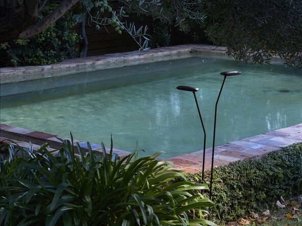 Zwei schlanke Bover Birdie Außenleuchten zwischen Pflanzen an einem Pool