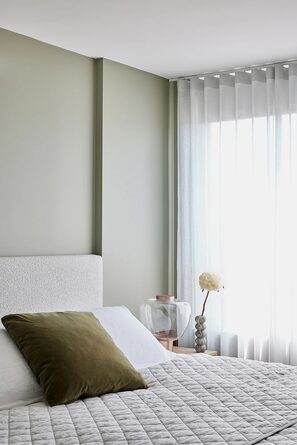 Schlafzimmer mit grüner Wand, hellem Bett und Riflesso am Fenster